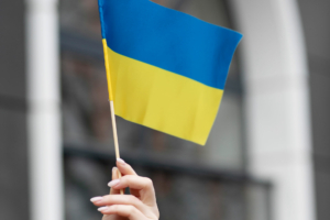 Hand hält kleine ukrainische Flagge in Blau und Gelb an einem Stab im Freien.