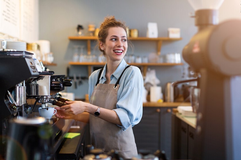 Mitarbeiterin in der Gastronomie, die lächelnd eine Kaffeemaschine bedient.