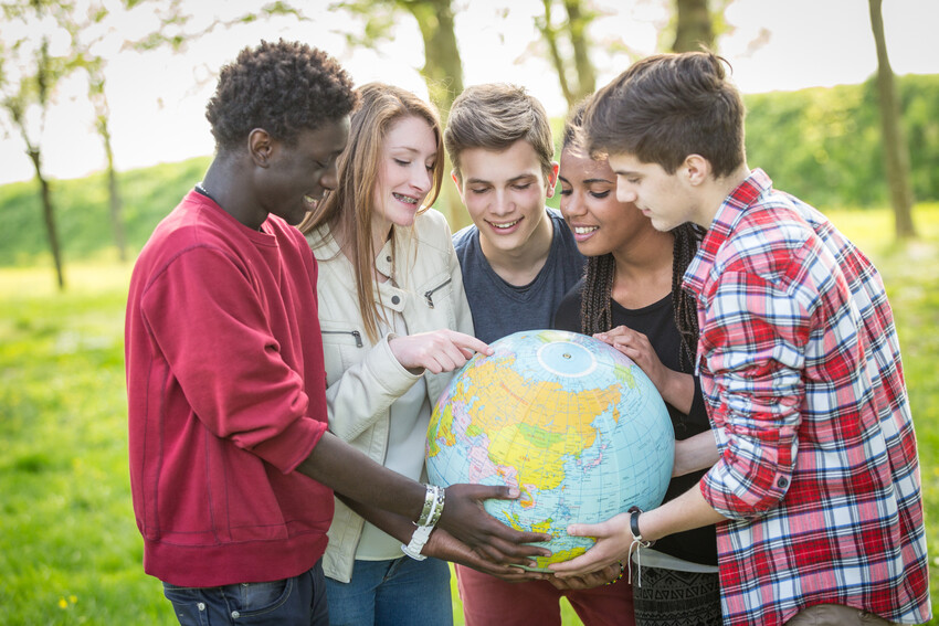 Mehrere Jugendliche mit verschiedenen Migrationsgeschichten halten eine Weltkugel im den Händen und schauen sich die Länder darauf an.